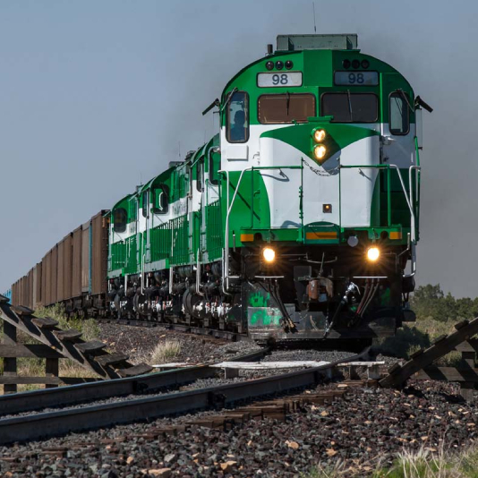 Apache Railway locomotive viewed from the yard at dusk, showing headlights and warm sunset glow. Photo copyright Patrick Phelan, used by permission.